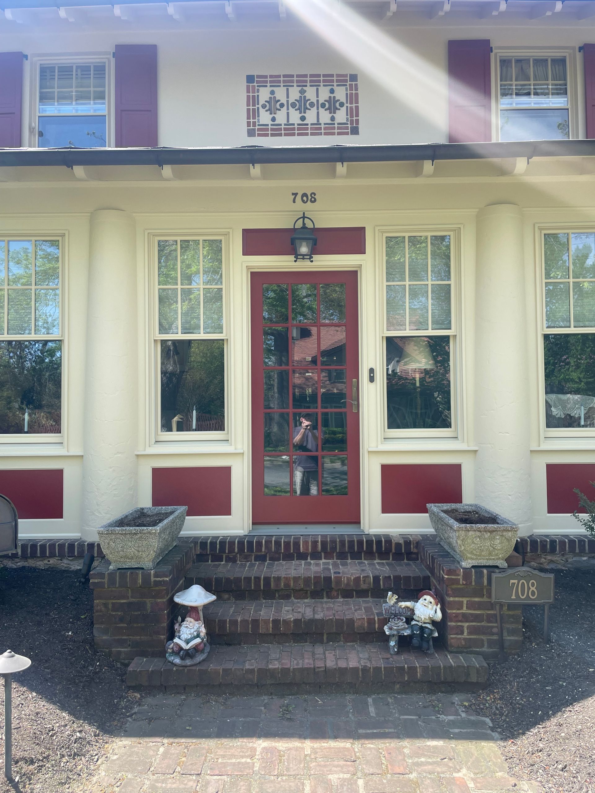 Red door and trim of a cream-colored house with red shutters. Brick steps lead to the entrance.