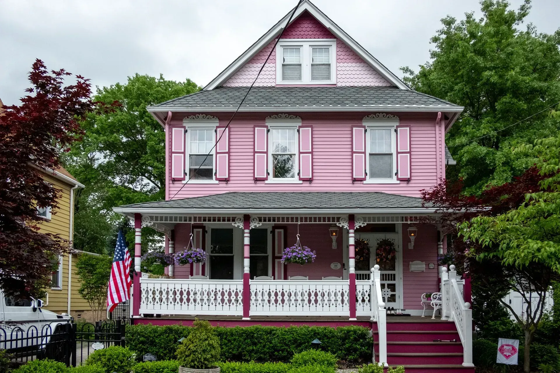 Two-story pink Victorian house with white porch, shutters, and American flag.