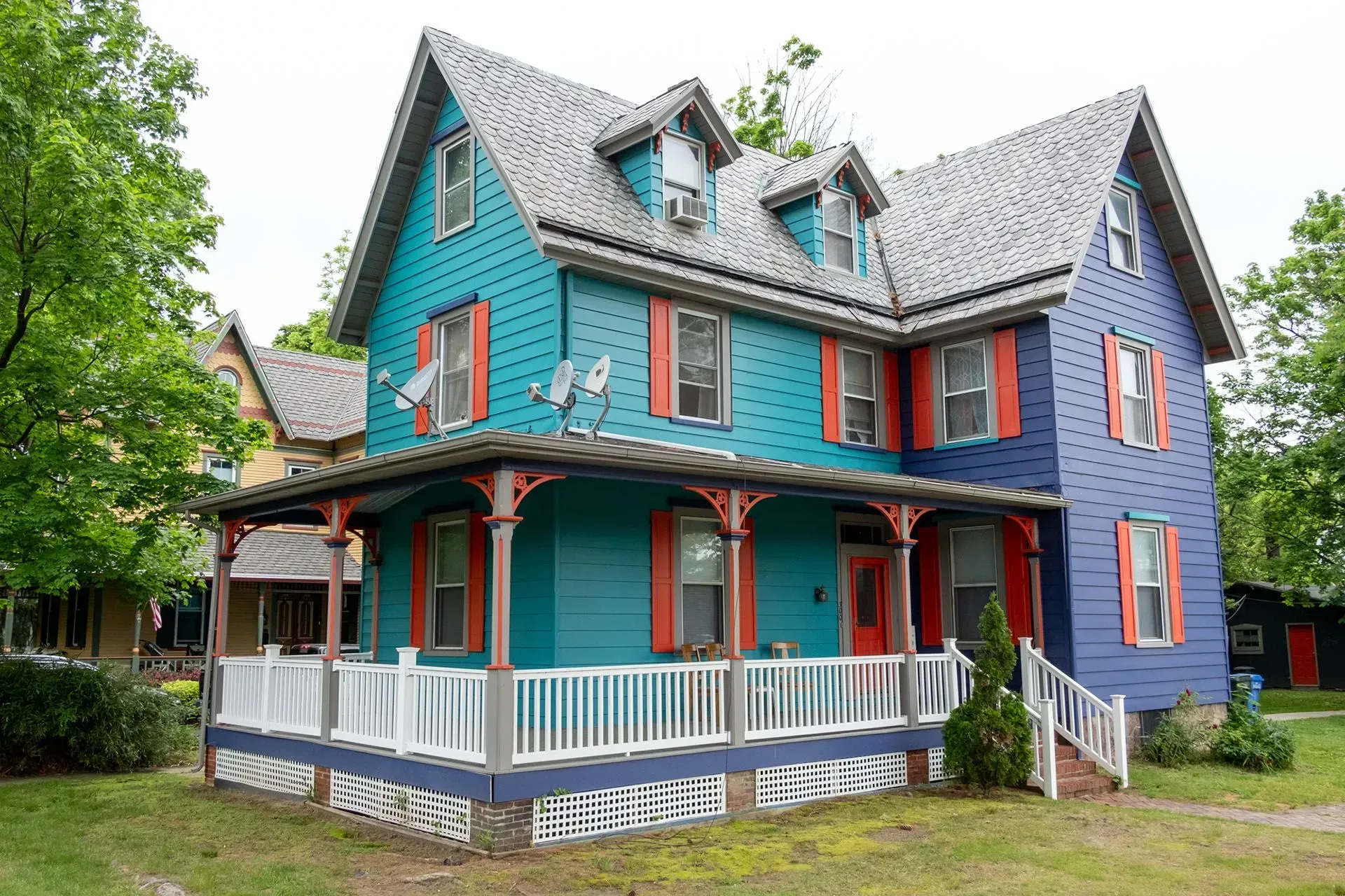 Colorful two-story house with teal and blue siding, red shutters, and a porch with white railing.