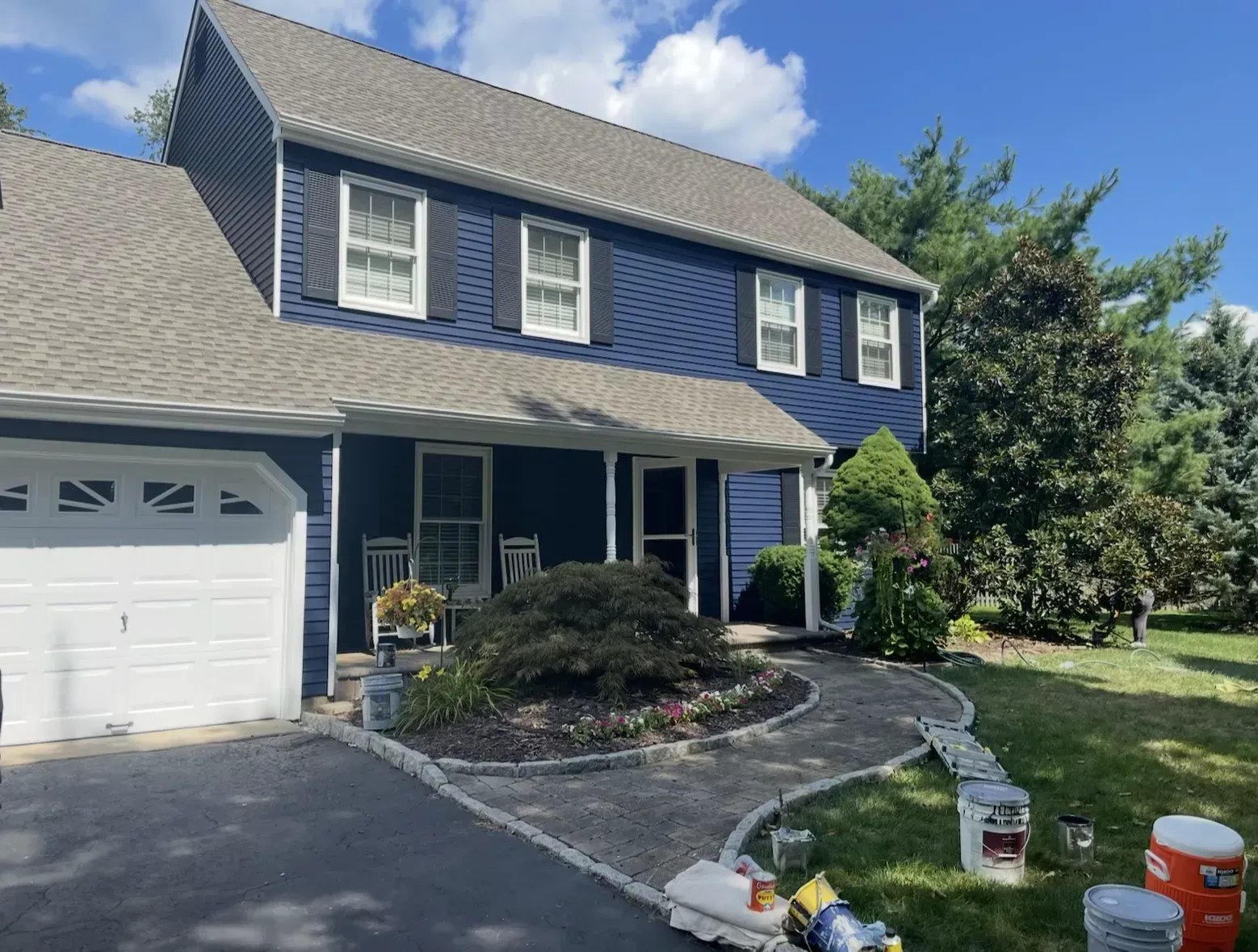 Blue house with white trim, gray roof, and stone walkway on a sunny day.