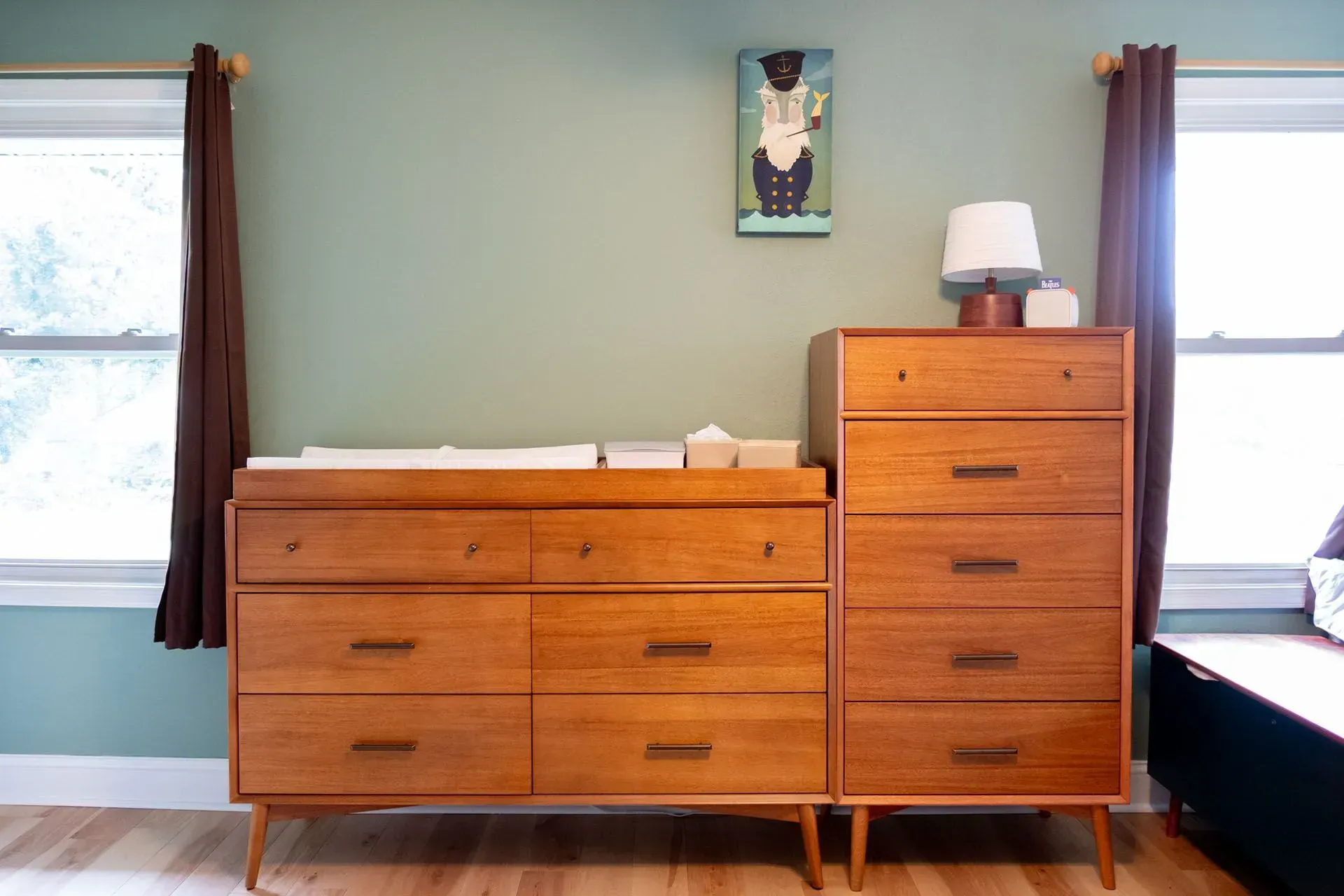 Wooden dresser and changing table against a green wall, with windows on either side.