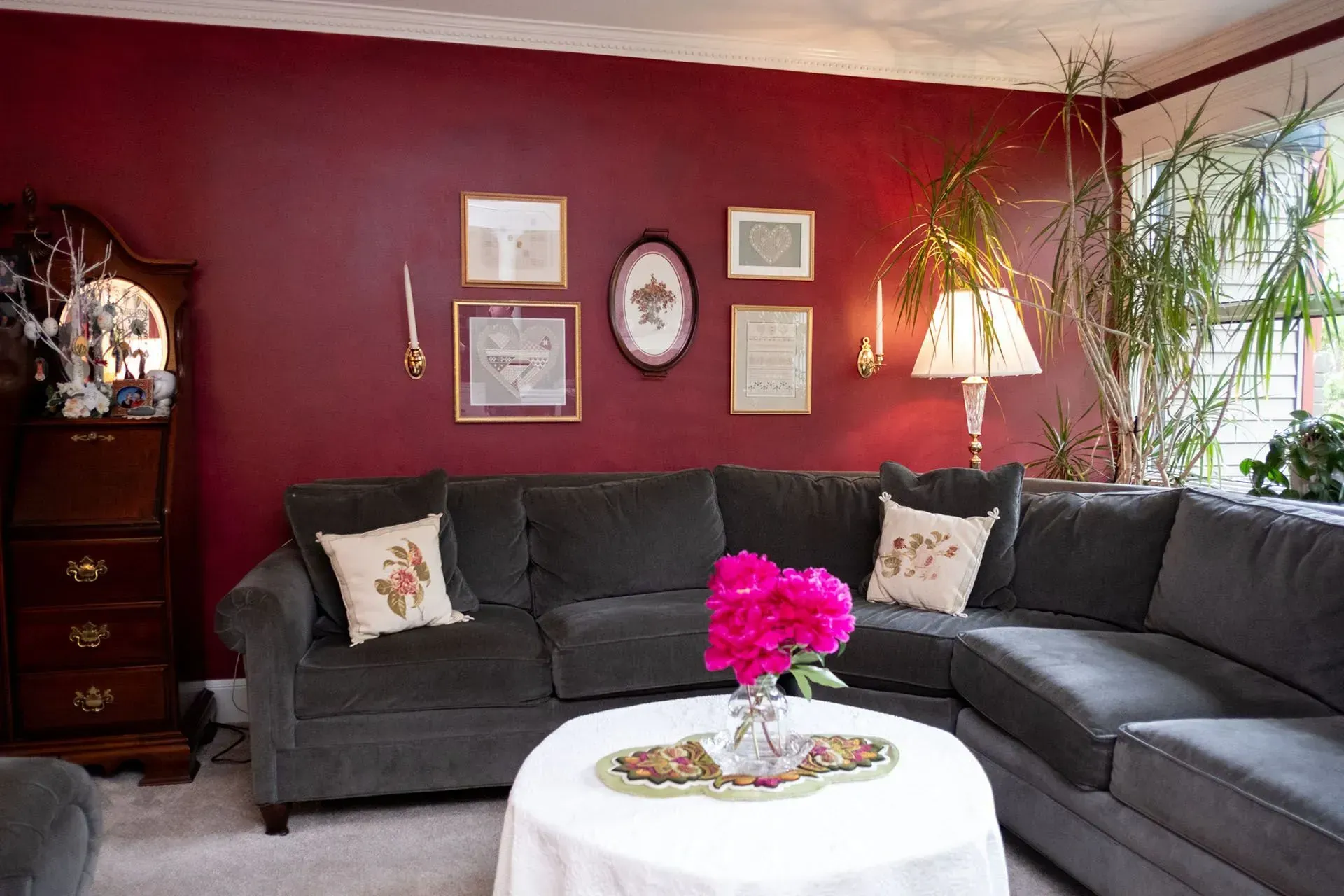 Living room with dark red wall, gray sectional sofa, art, and white round table.
