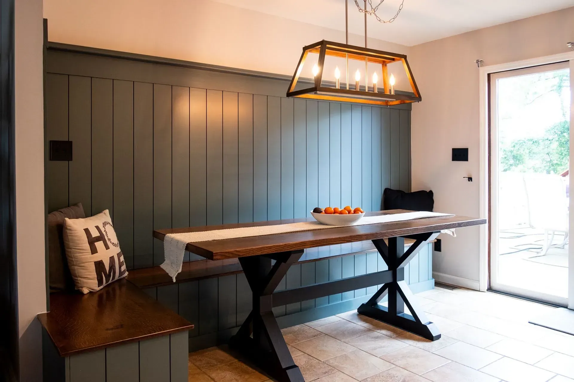 Dining area with teal wall paneling, wooden table, bench seating, and a large light fixture.