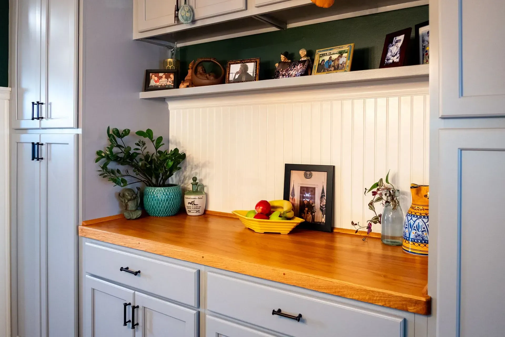 A light-filled kitchen nook with a wood countertop, white beadboard, and gray cabinets.
