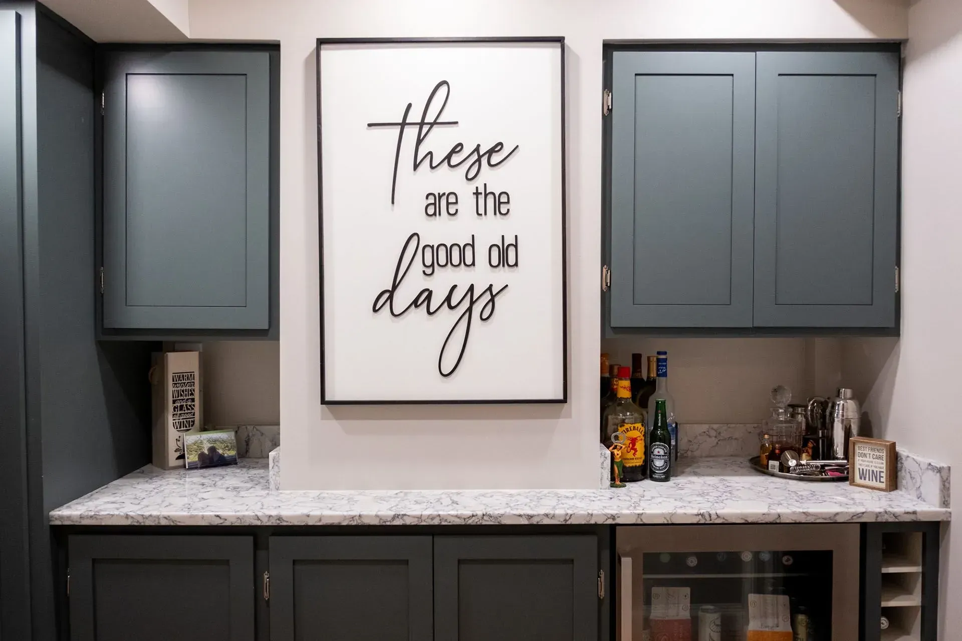 A home bar with blue cabinets, granite countertops, and a framed sign that reads 