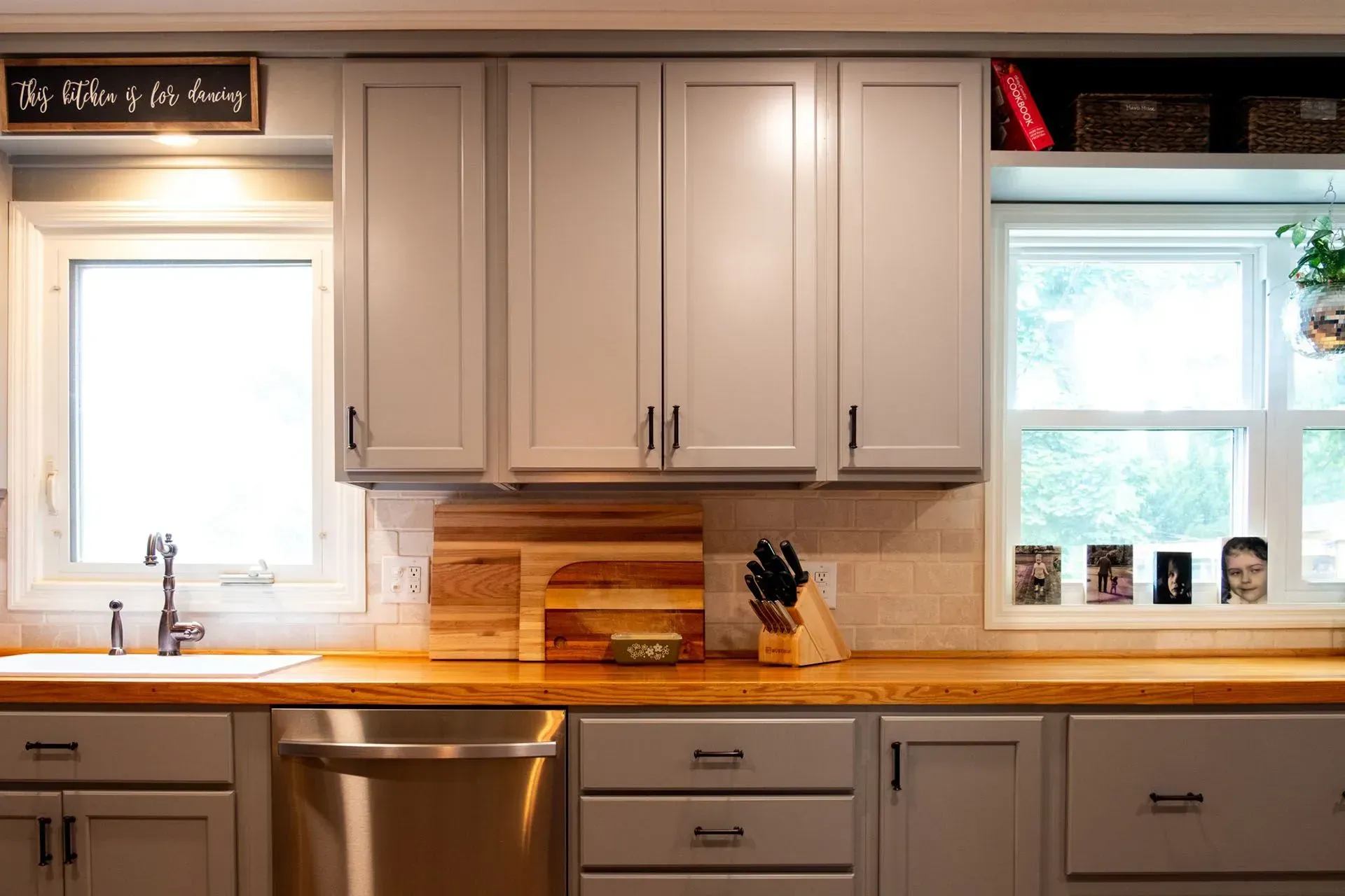 Kitchen with gray cabinets, wood countertop, stainless steel appliances, and two windows.