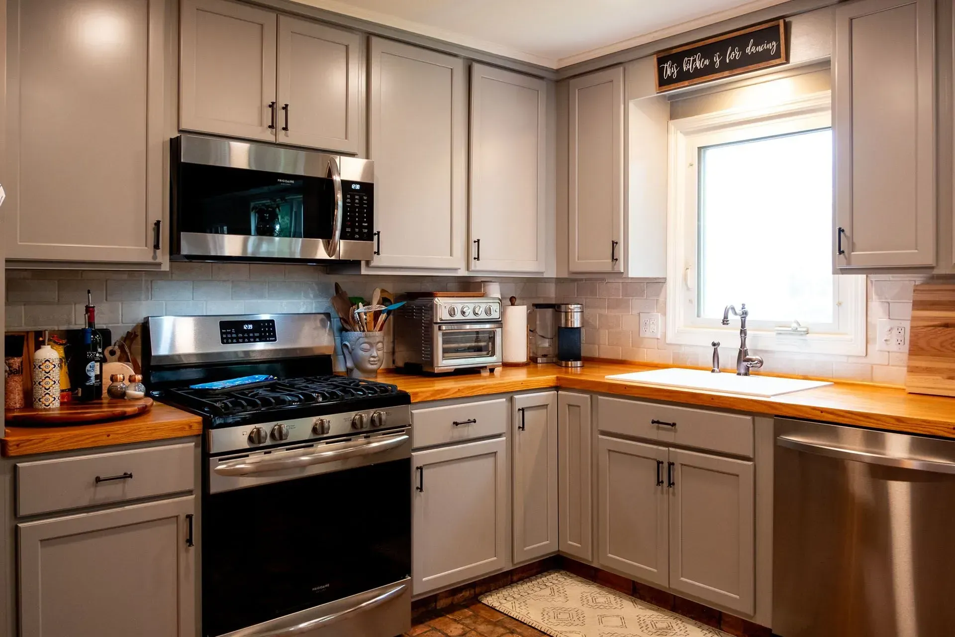 Gray kitchen cabinets with stainless steel appliances and wood countertops.