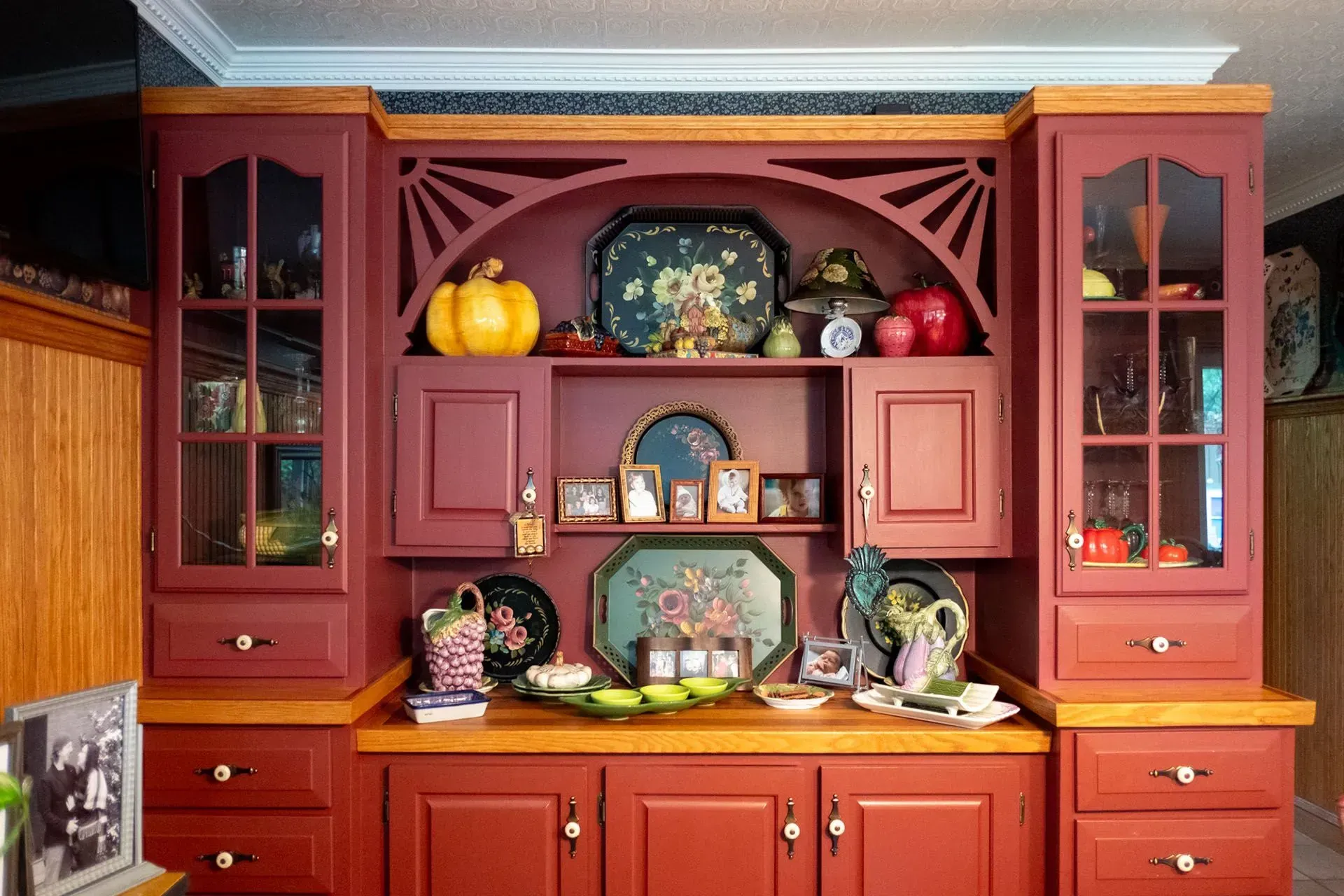 Red and wood hutch decorated with fall items, with glass-doored cabinets and various decorative trays.