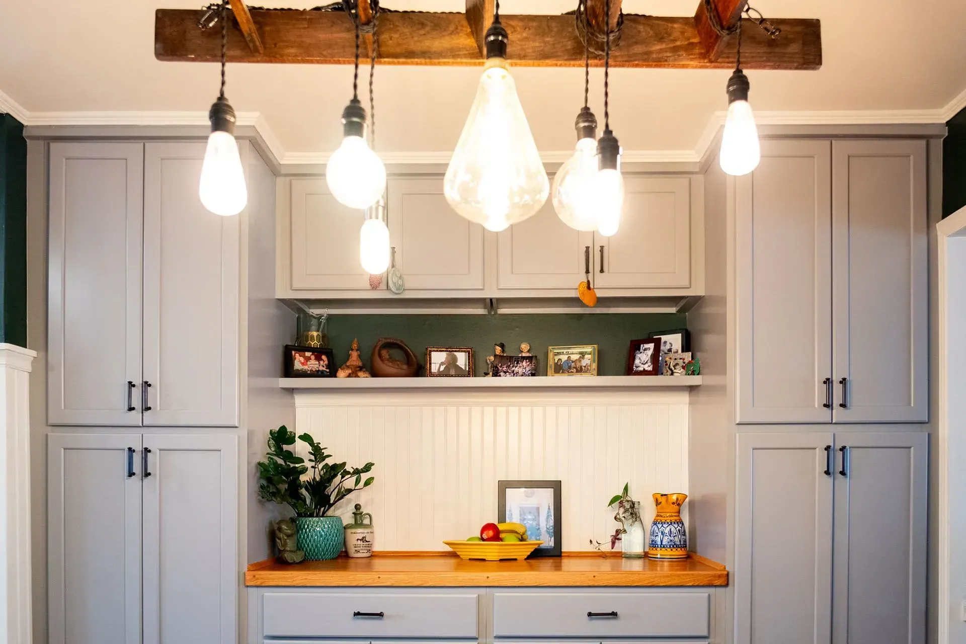 Gray kitchen cabinets with wood countertops, shelving, and hanging light fixtures.