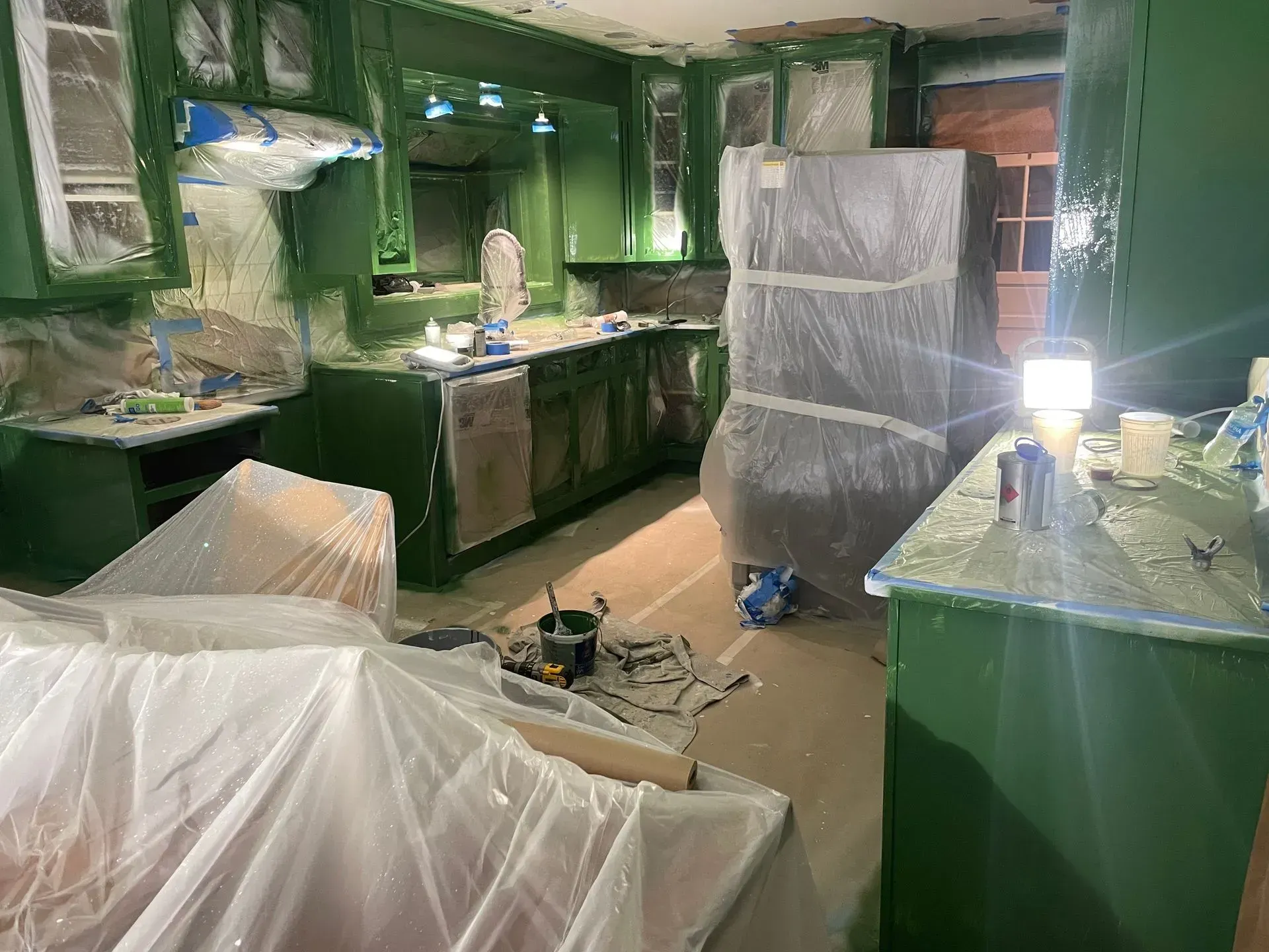 A kitchen under renovation, cabinets and walls painted a bright green, appliances covered in plastic sheeting.
