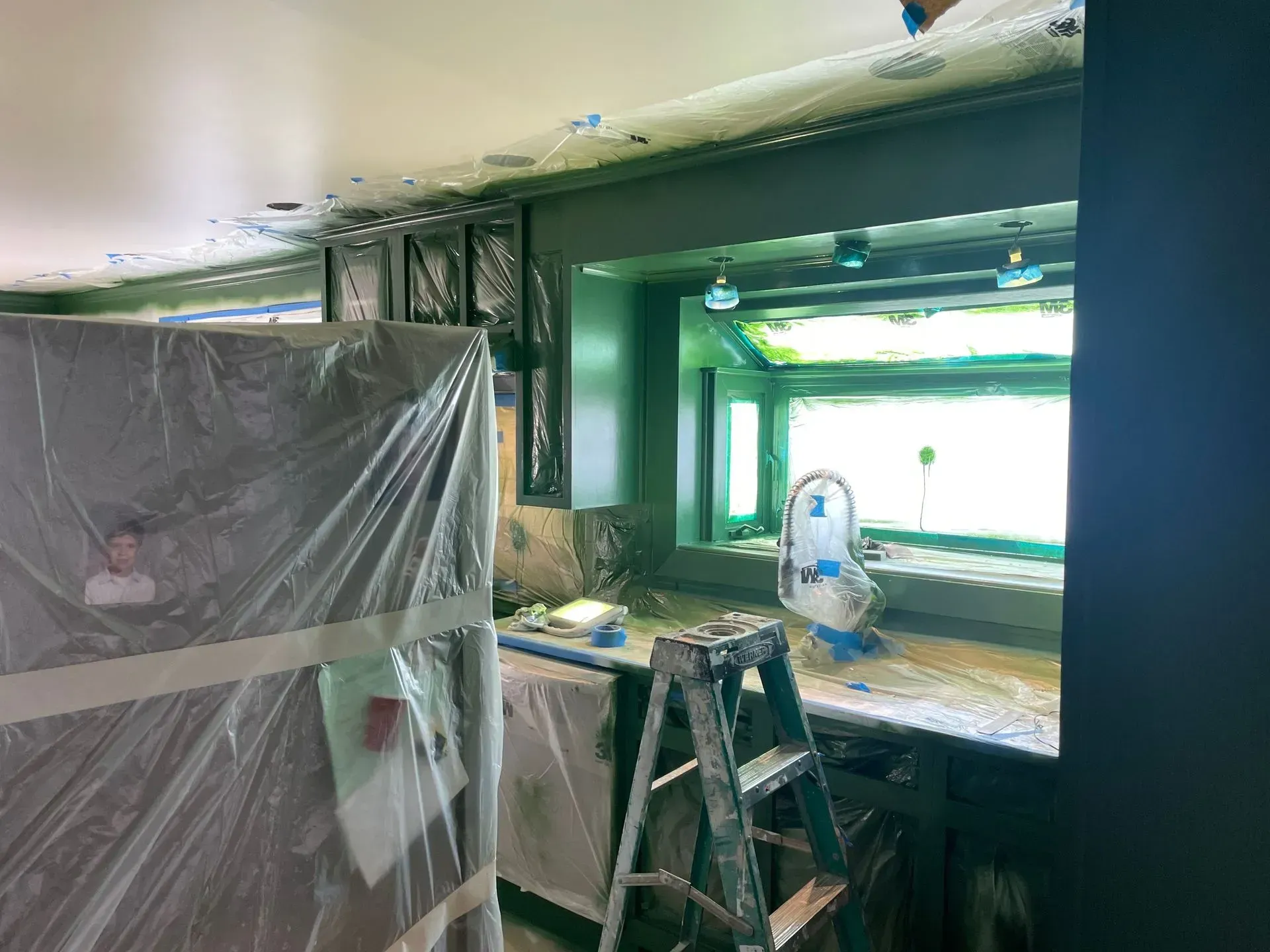 Interior room under renovation with covered furniture, green window frame, and a ladder.