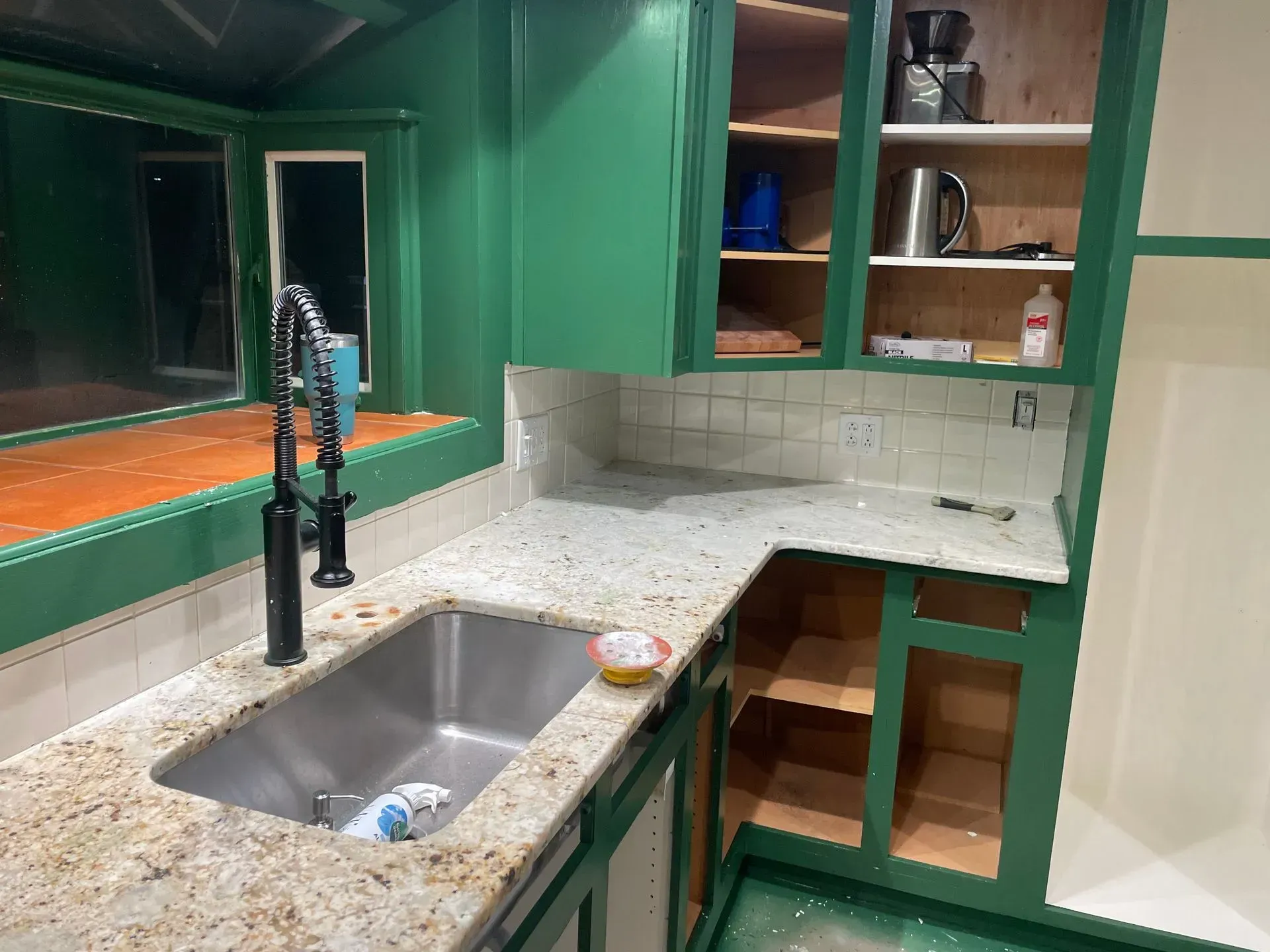 Green kitchen cabinets, granite countertops, stainless steel sink. Construction in progress.