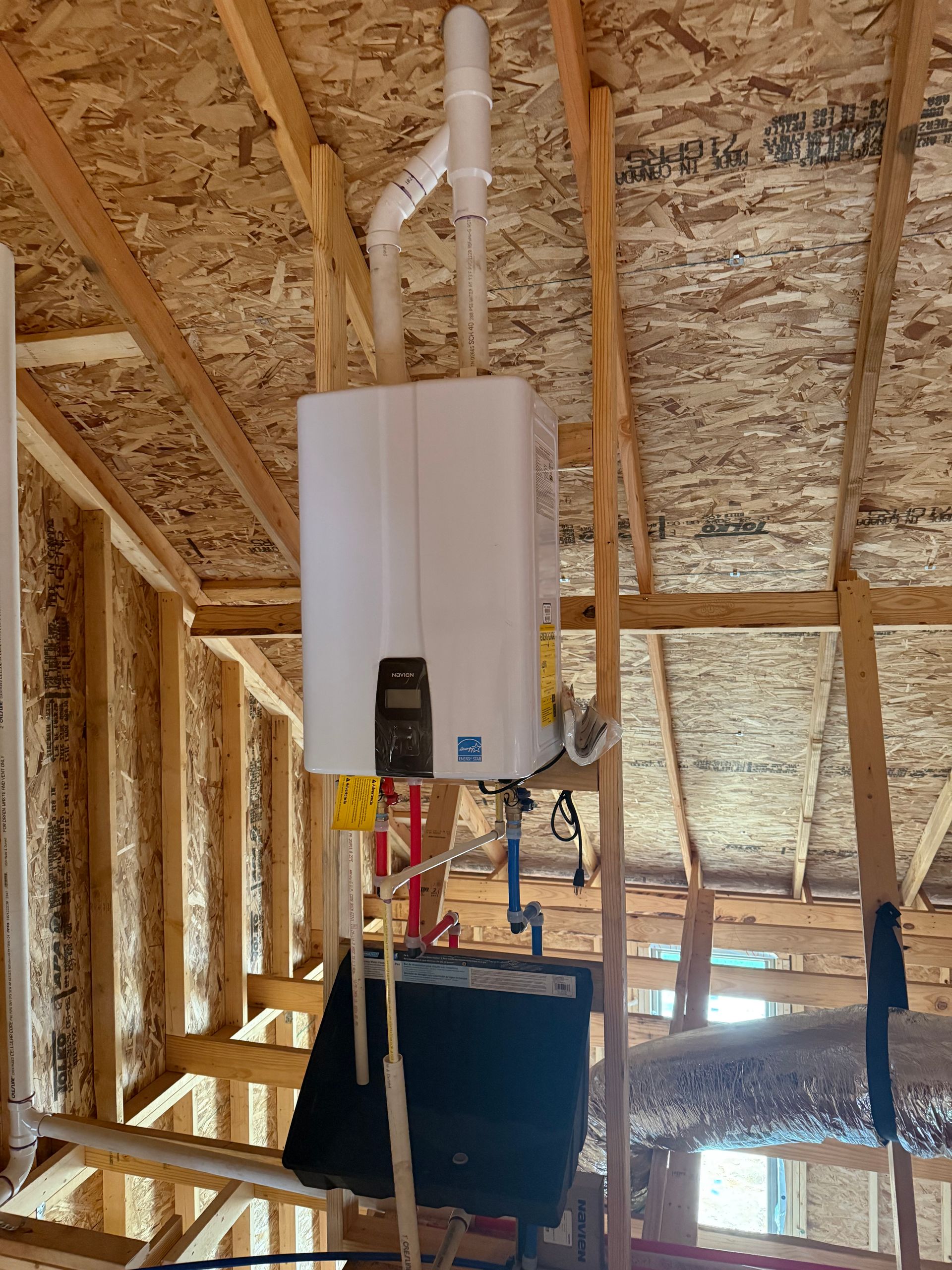 A white water heater is hanging from the ceiling of a house under construction.
