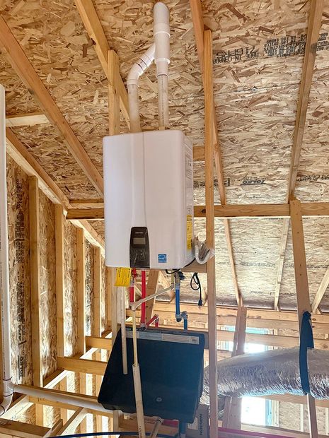 A white water heater is hanging from the ceiling of a house under construction