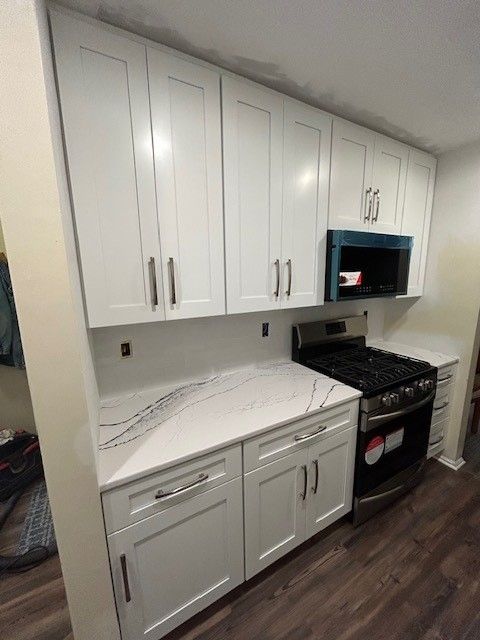 A kitchen with white cabinets, a stove, and a microwave