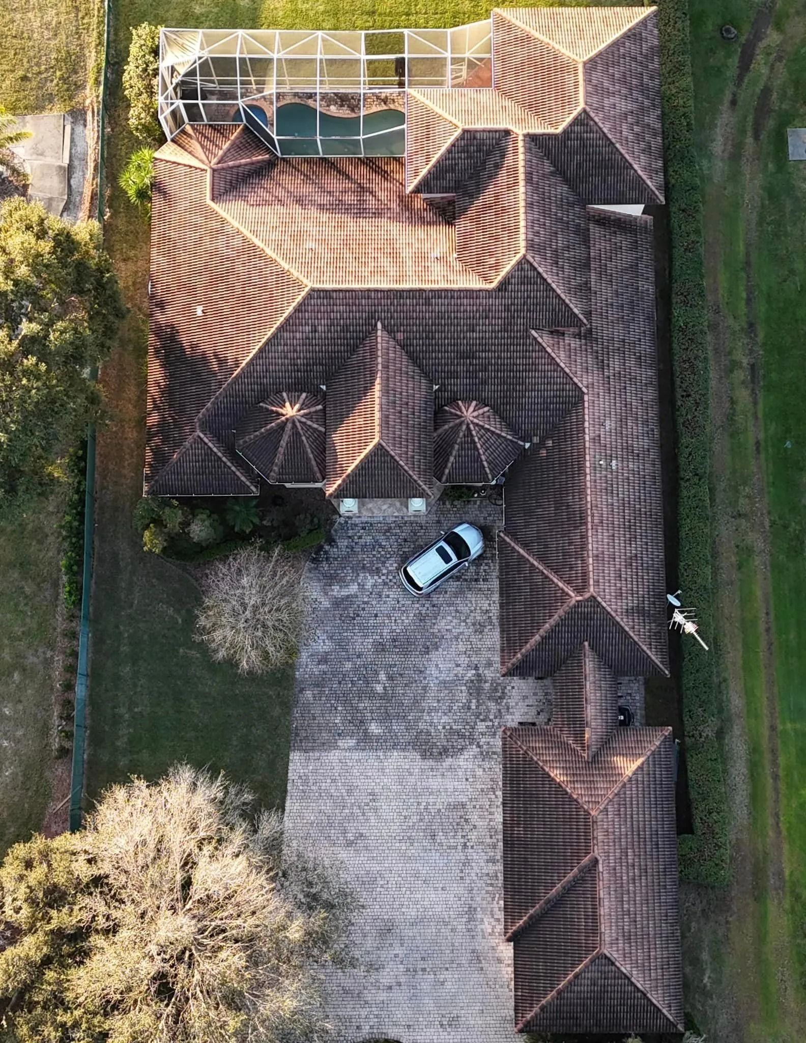 Overhead view of a house with a tiled roof, a car parked in the driveway, and a swimming pool.