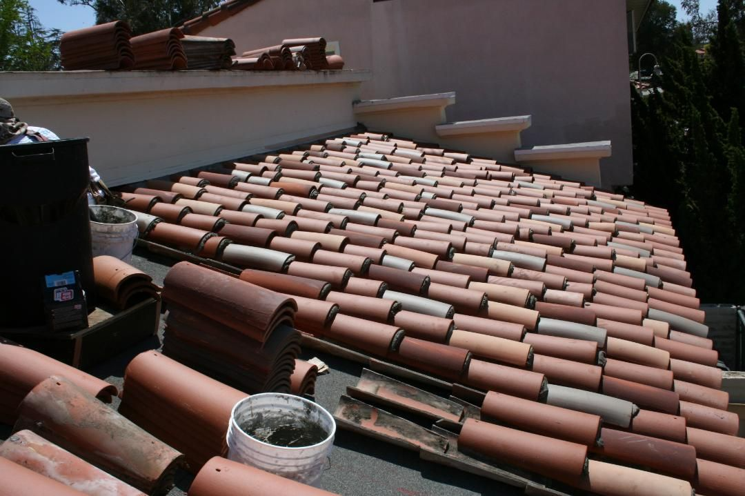 Terracotta tile roof with partial tiles laid. A white bucket sits on the edge.