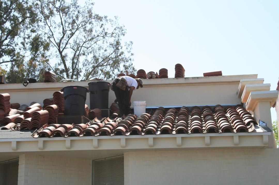 Man installing terra-cotta roof tiles on a beige building. Sunlight.