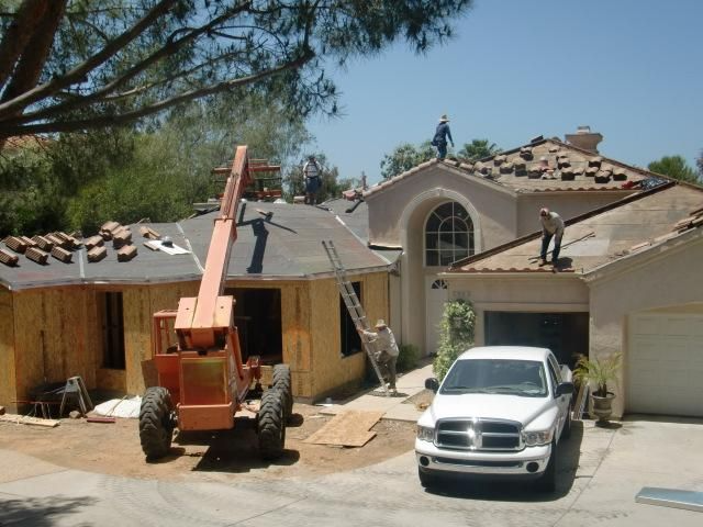 Roofers working on a residential roof, using a forklift and ladder. White truck parked in the driveway.