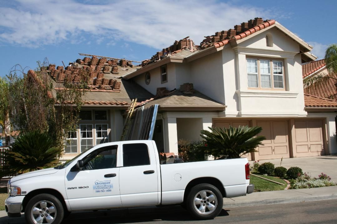 White truck parked in front of a house with roof tiles piled on the roof during a repair.