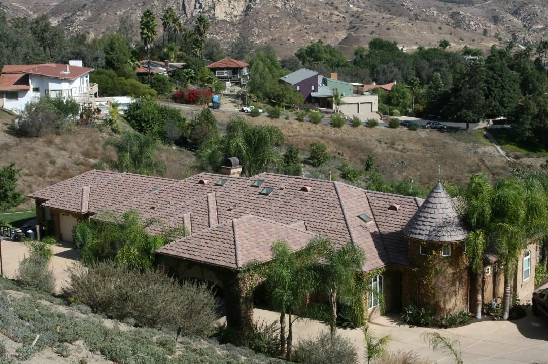 Houses nestled in a hillside with tile roofs and a turret, surrounded by trees and greenery.