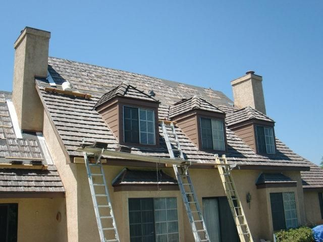 Roof replacement in progress on a stucco house, with ladders, dormers, and chimneys.