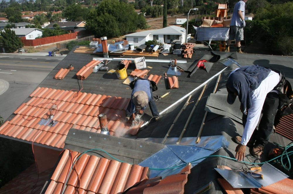 Roofers working on a residential roof, cutting tiles and installing new ones, sunny day.