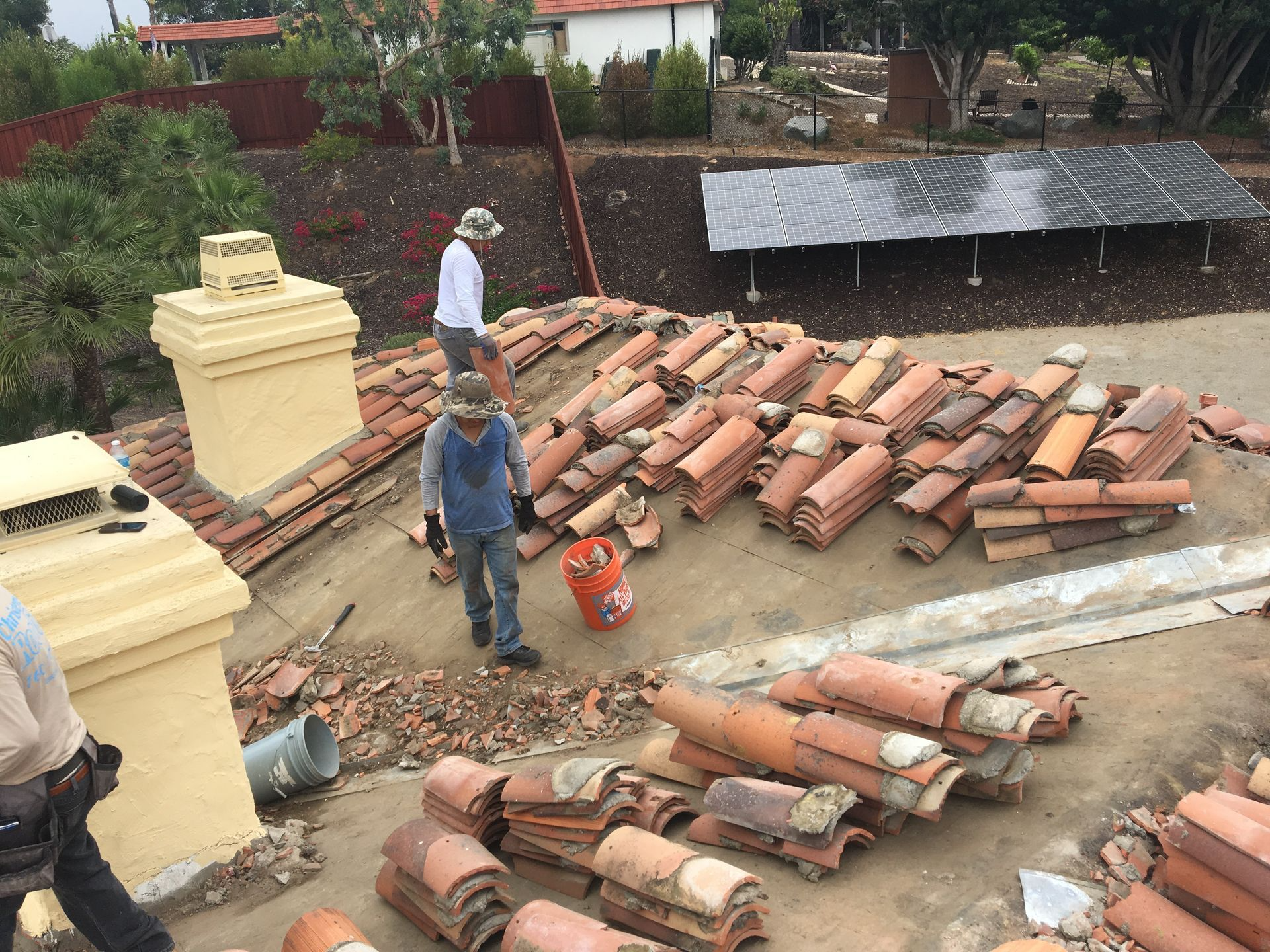 Roofers removing clay tiles from a rooftop. Two men stand near stacks of terracotta tiles.