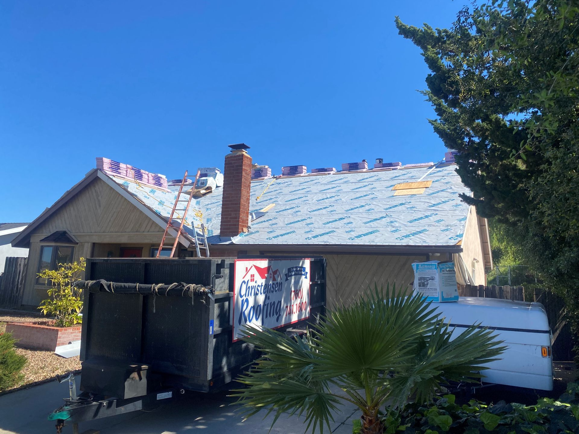 House being re-roofed: tar paper laid, truck with supplies, ladder, sunny day.
