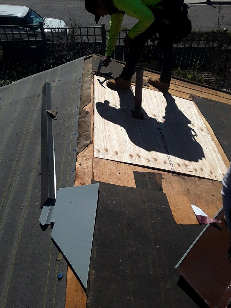 Roofer working on a roof, using a hammer near a chimney. Sunny day.