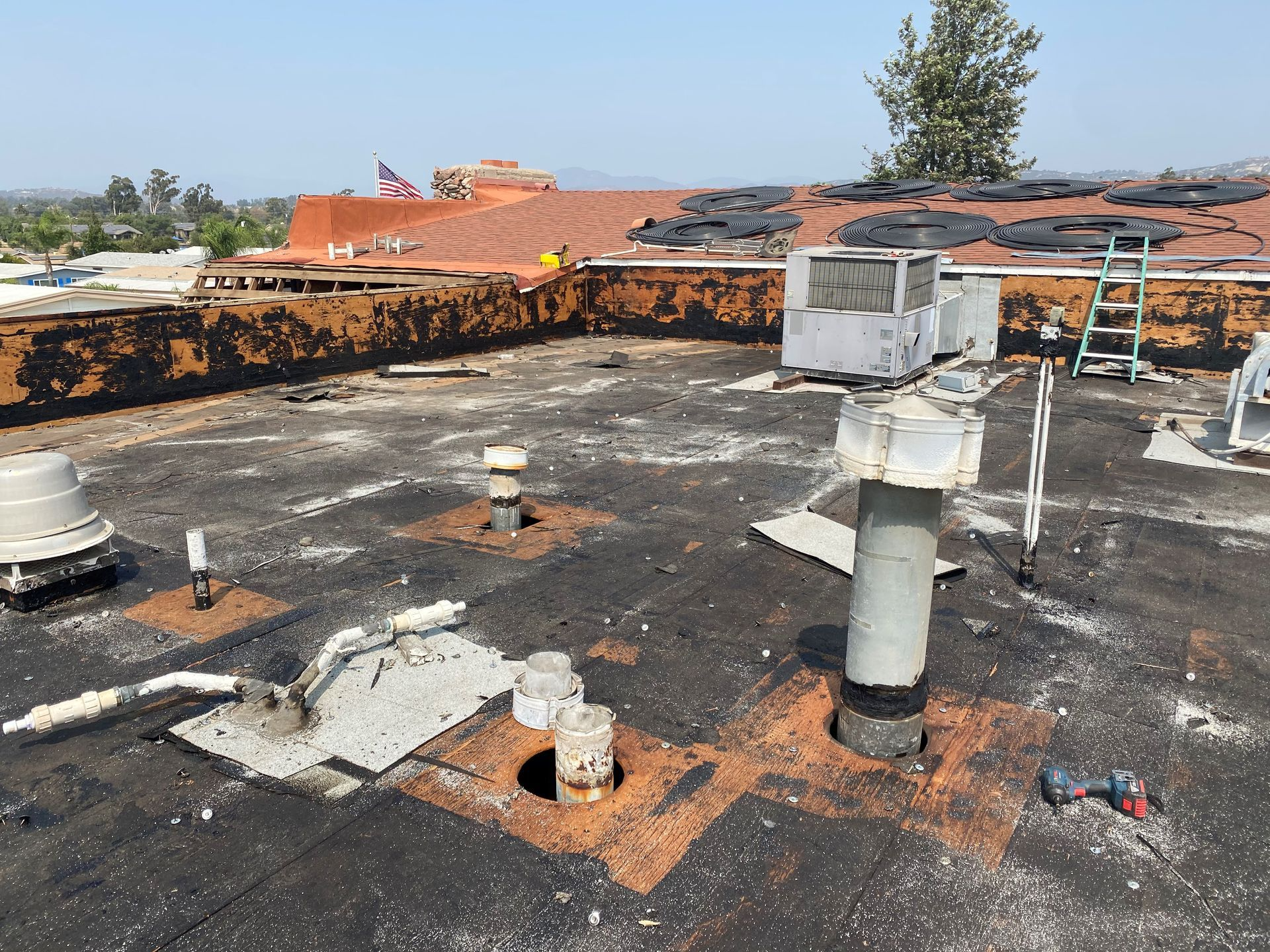A damaged, flat commercial roof with HVAC units, vents, and debris, scorched in black.