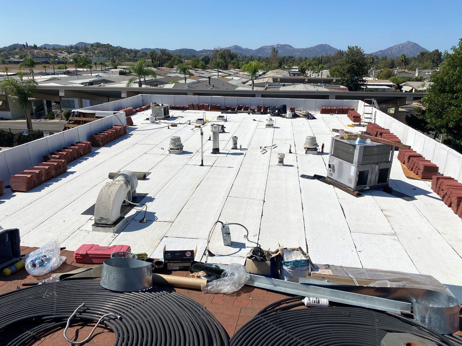 Rooftop with white surface, equipment, and red tiles. Clear sky, residential setting with mountains.