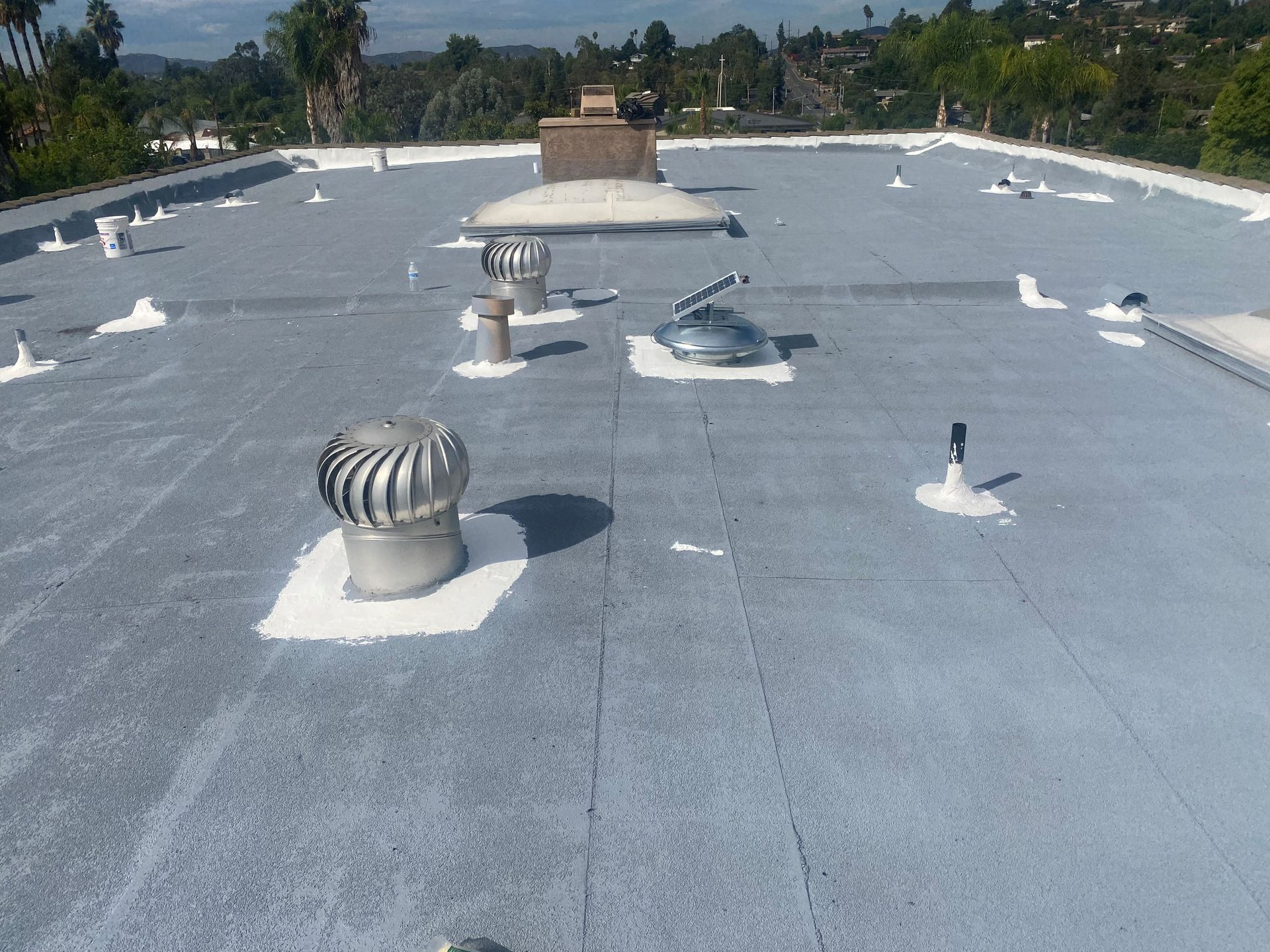 Flat roof with vents and skylights, painted gray with white sealant.