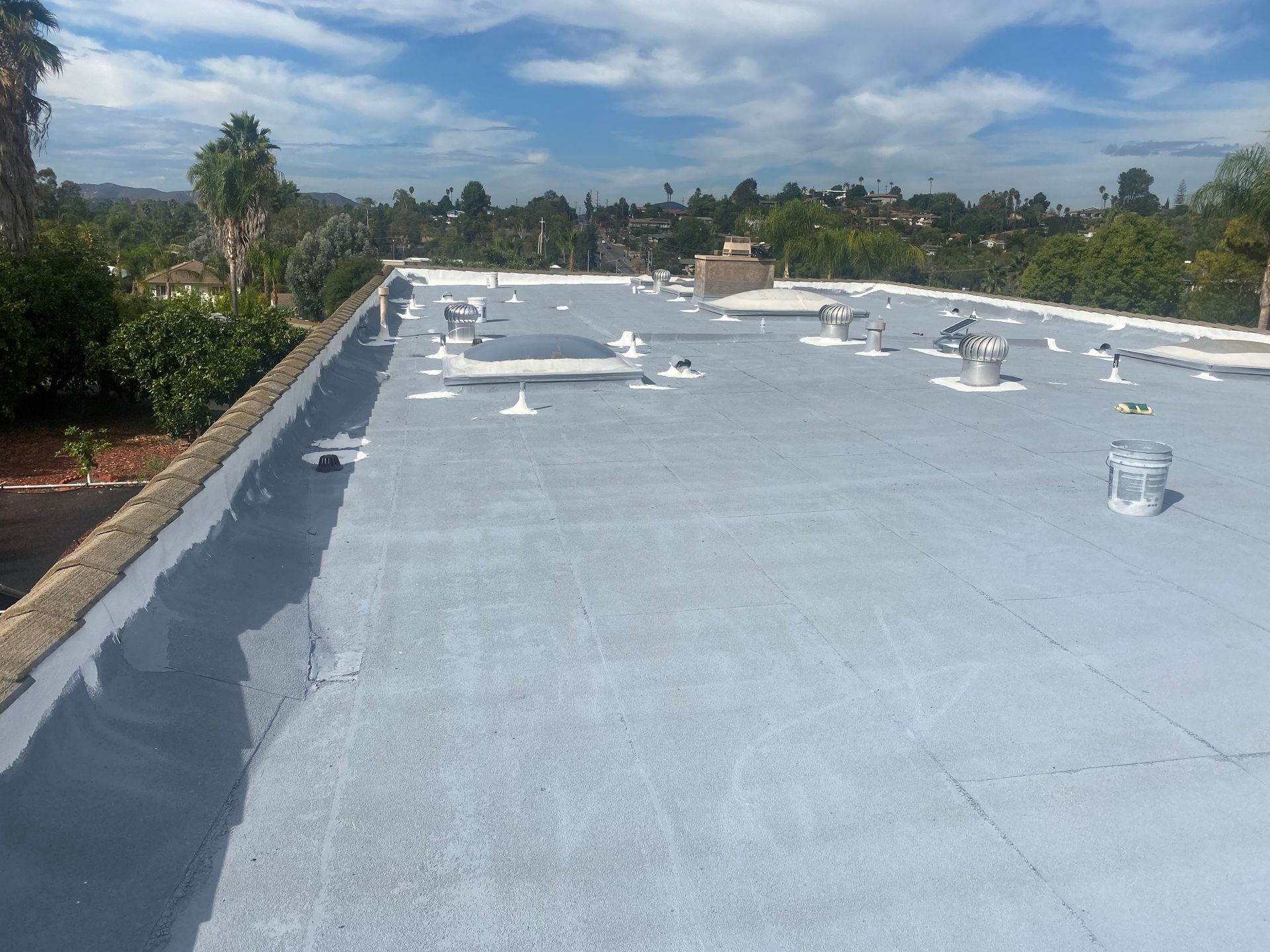 Flat commercial roof, freshly painted gray, with vents and a surrounding cityscape on a sunny day.