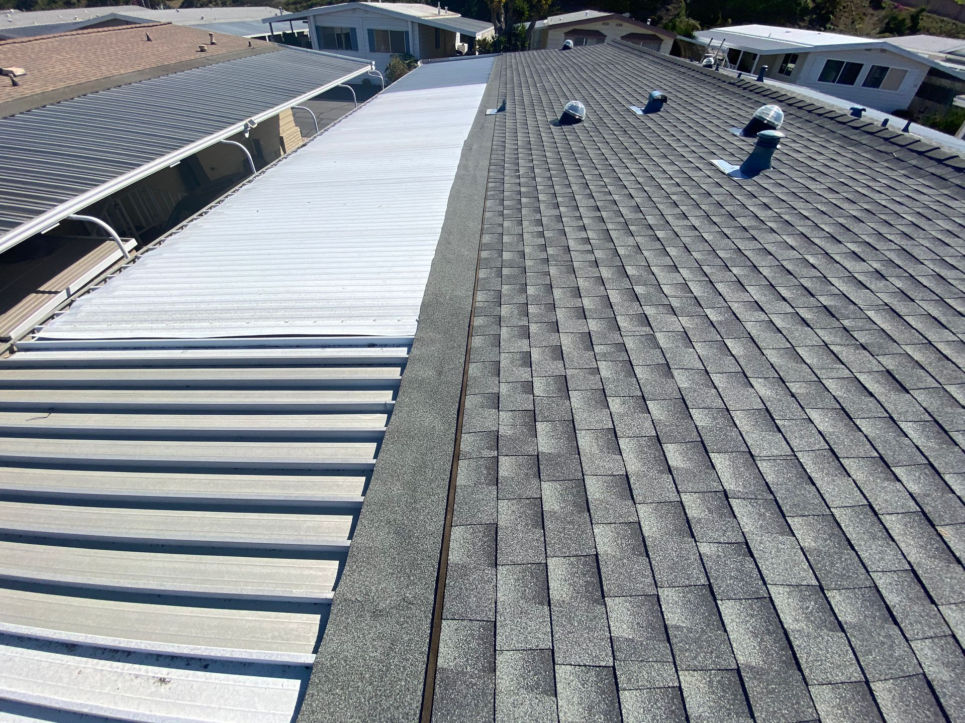 Roof with shingles and corrugated metal side-by-side. Gray, white, and blue. Sunny day.