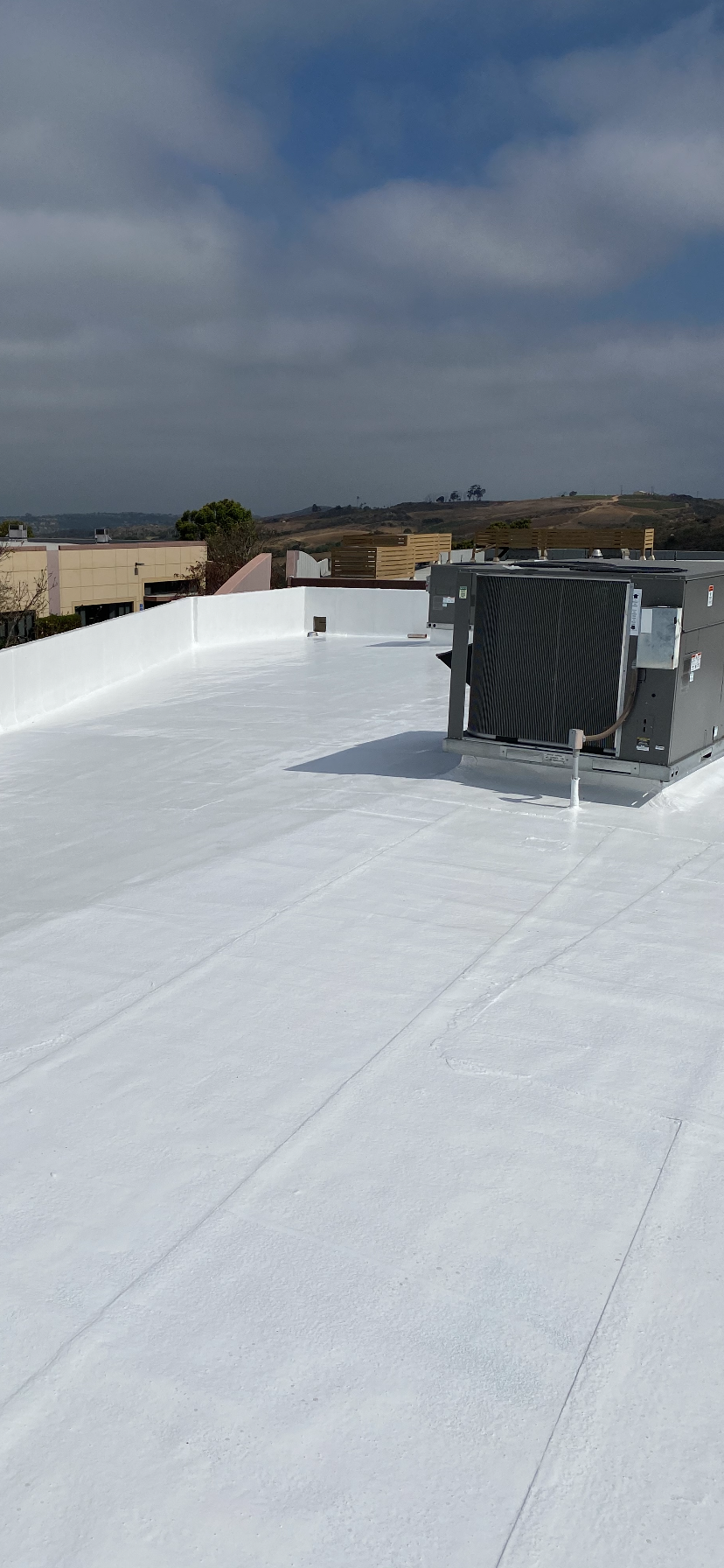 White commercial roof with HVAC units against a cloudy blue sky.