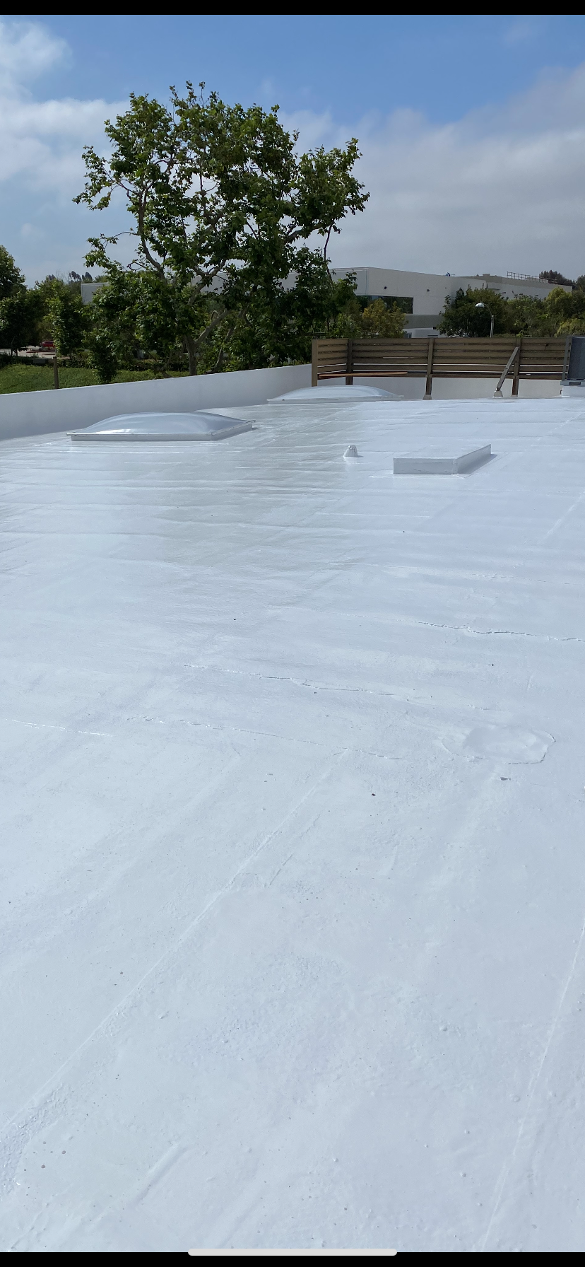 White-coated flat roof with a cloudy sky, trees, and a fence in the background.