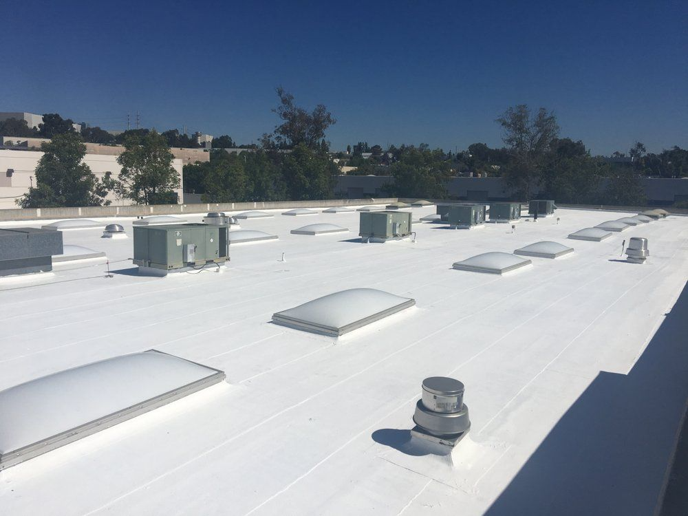 White commercial roof with skylights and air conditioning units under a blue sky.