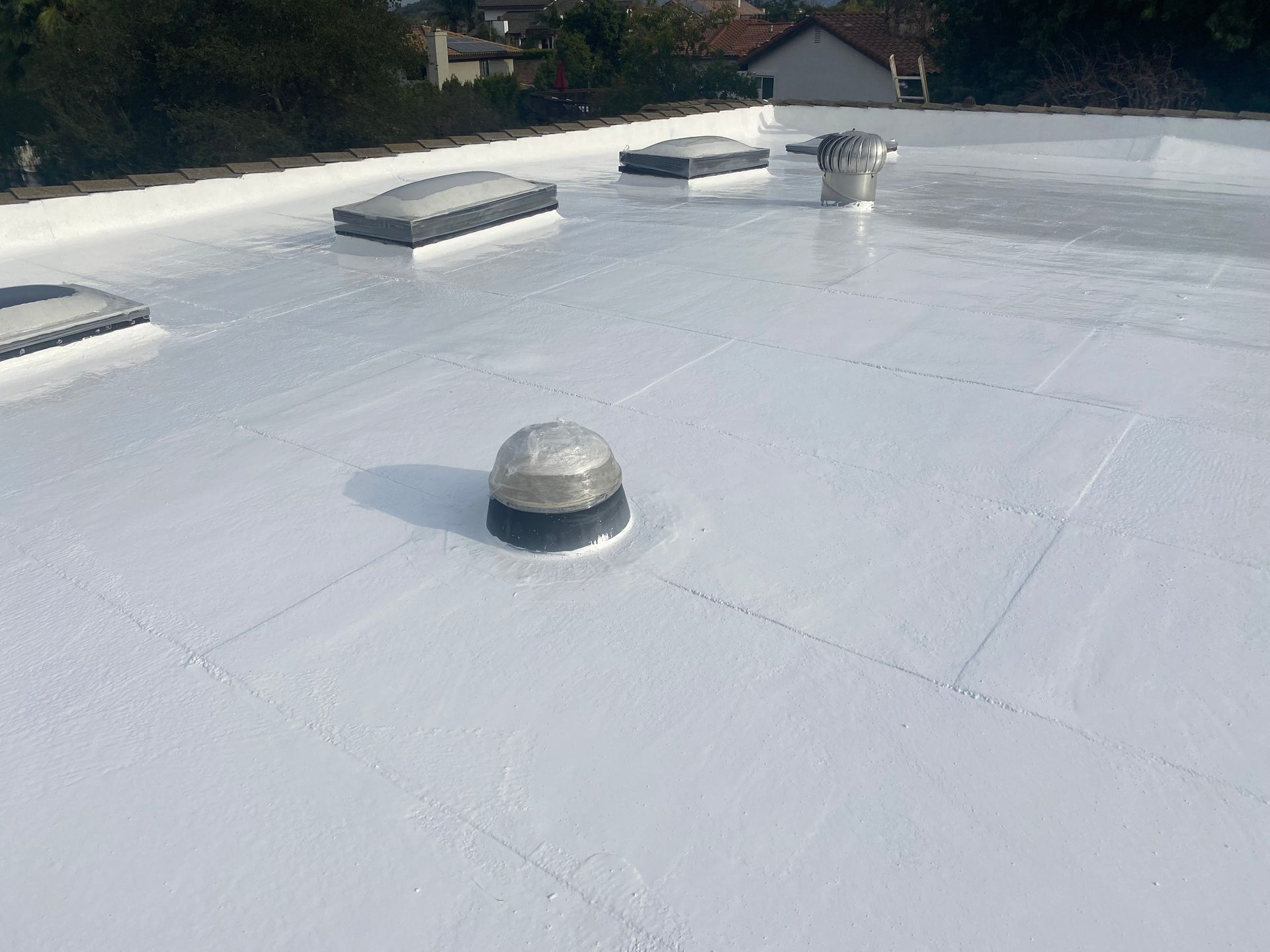 White-coated flat roof with skylights and vents, reflecting sunlight.