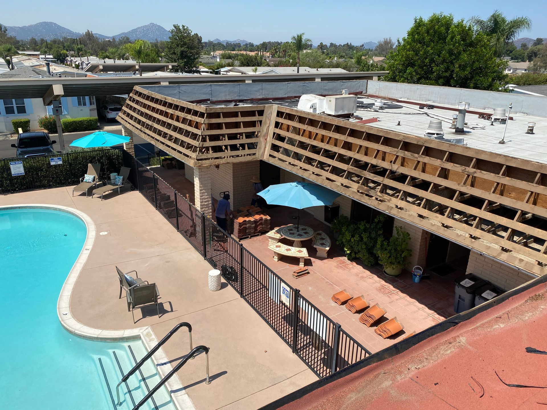 Poolside view of a building with a wooden overhang. A person walks towards a patio with tables and chairs.