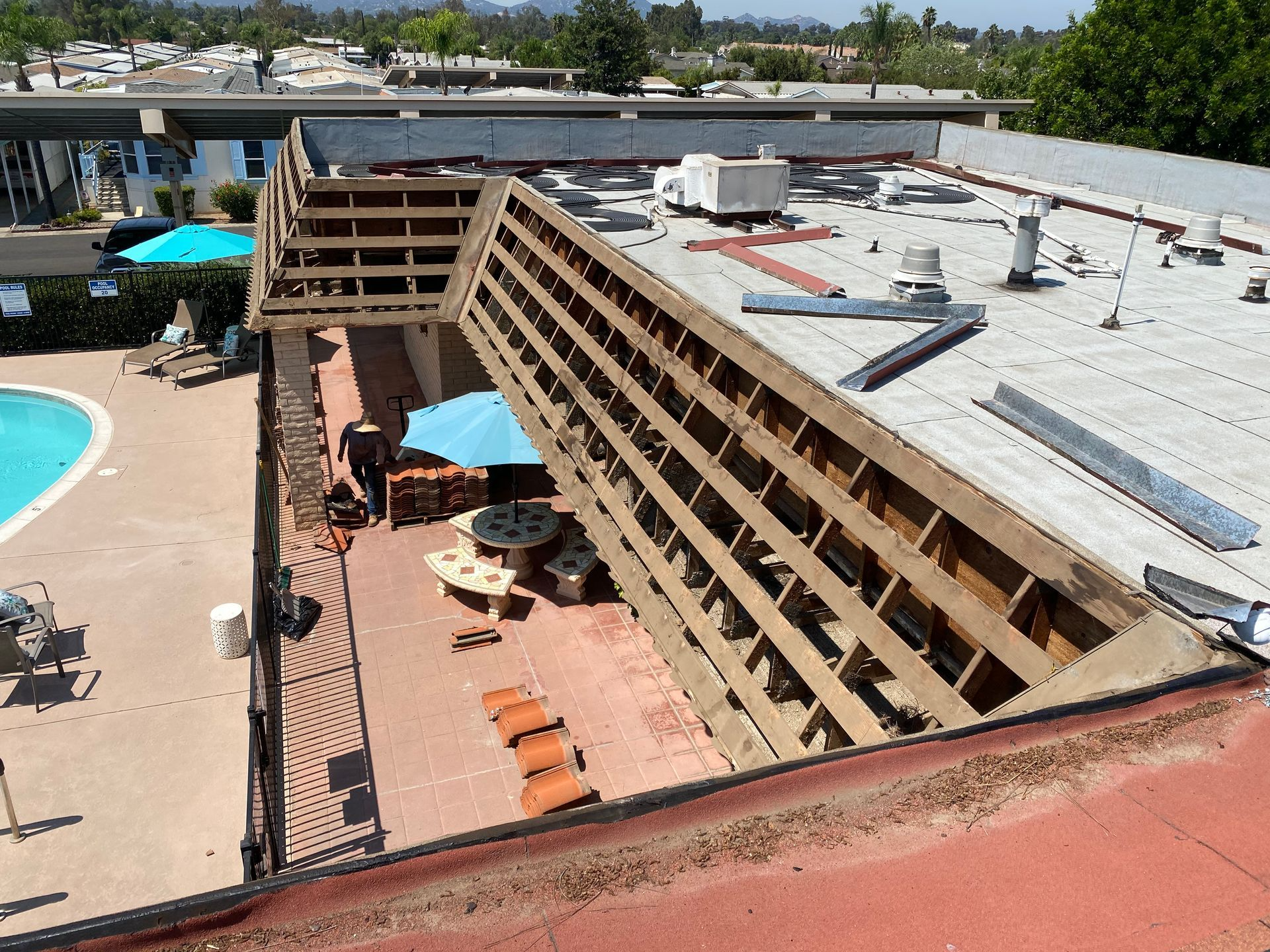 Exterior view of a building with a partial collapsed roof, revealing interior, near a pool and patio area.