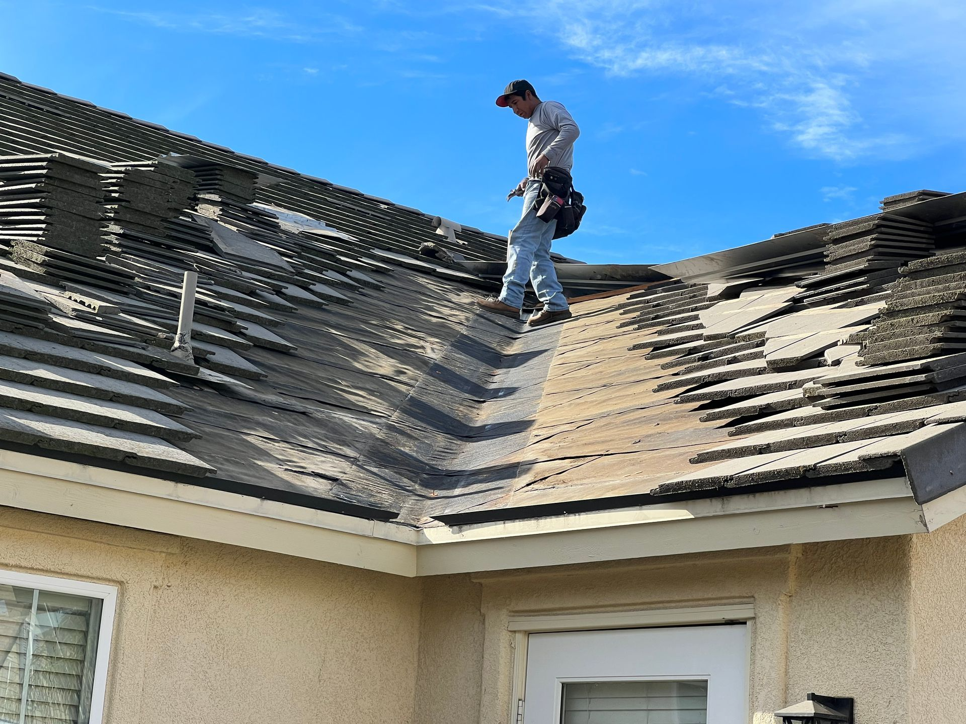 Man on a partially torn-off roof, preparing for repairs under a blue sky.