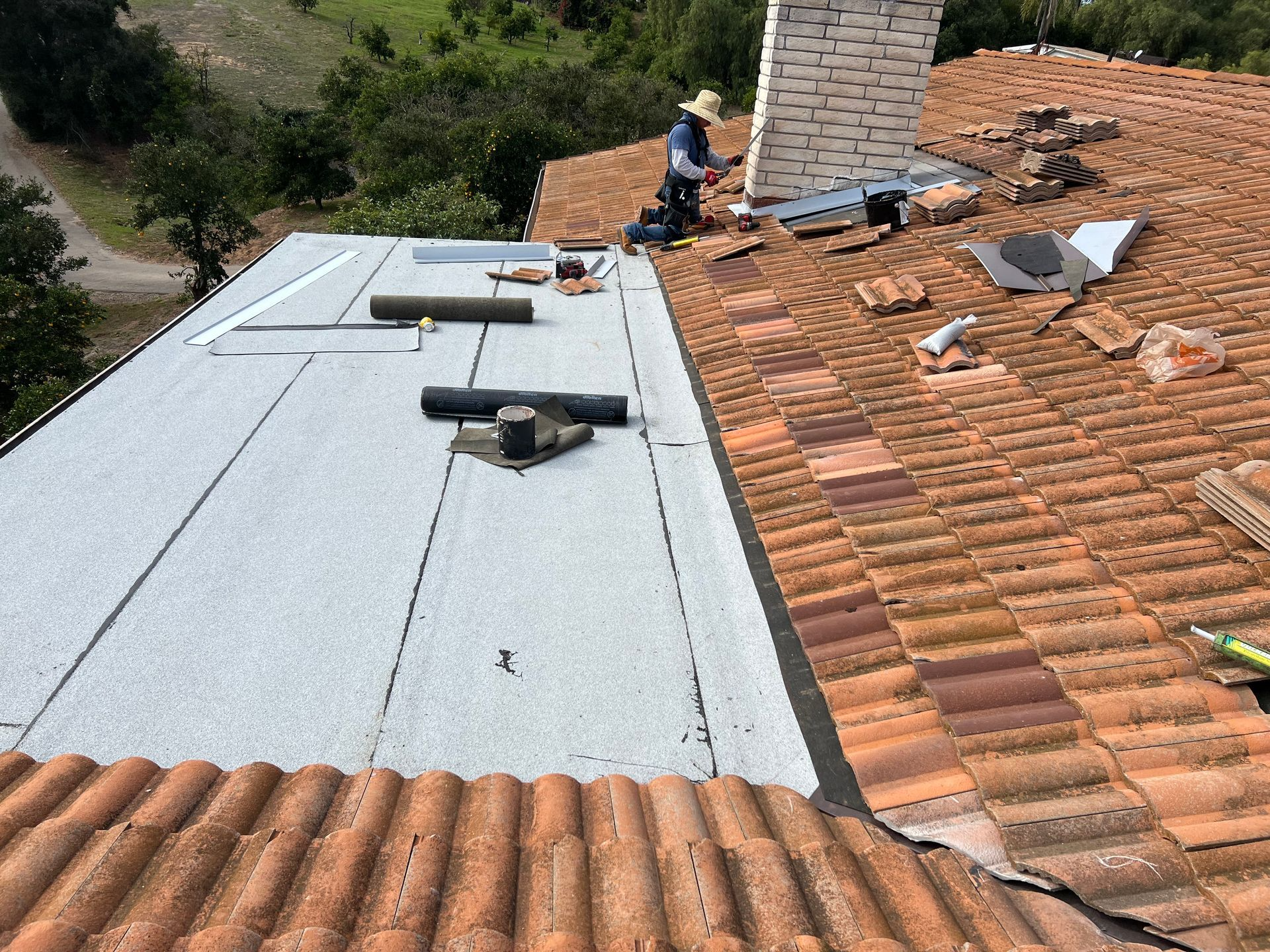 Roofer on a rooftop, installing new roofing material; terracotta tiles and flat, gray surface.