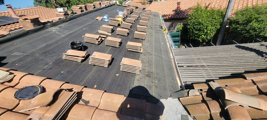 Roof repair, tiles and tools on a dark underlayment, sunny day.