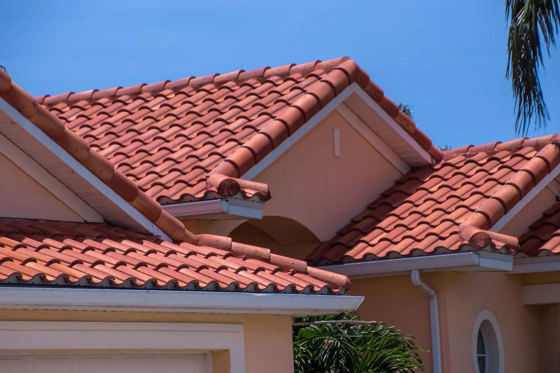 Red ceramic tile roof on a pale orange house against a blue sky.