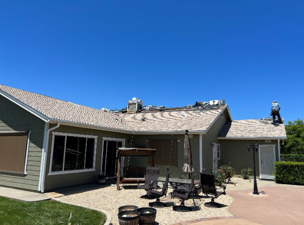 House with roof damage, a person working on the roof under a blue sky.
