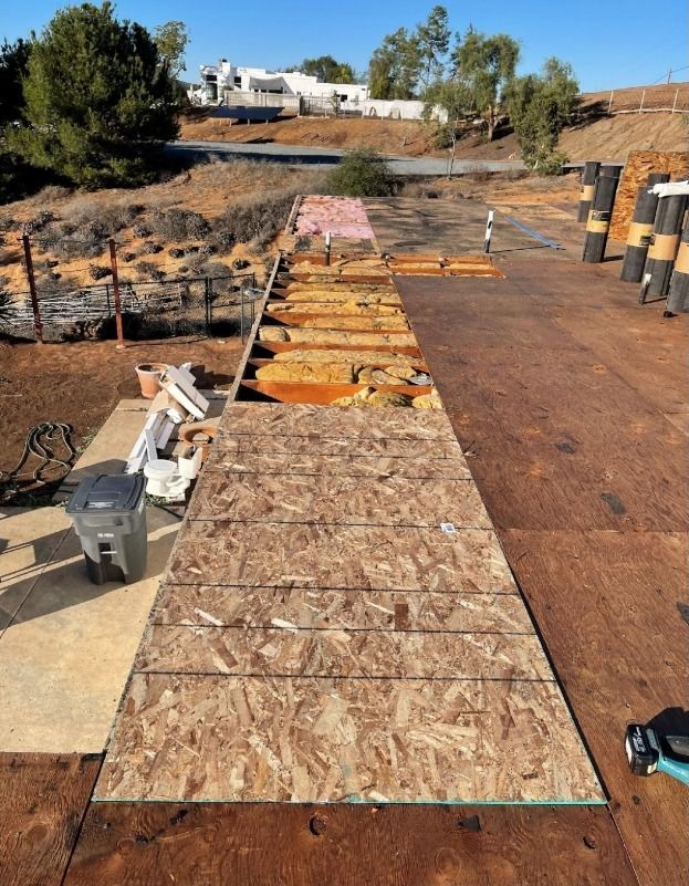 Roof under construction with exposed wood and materials; sunny day.