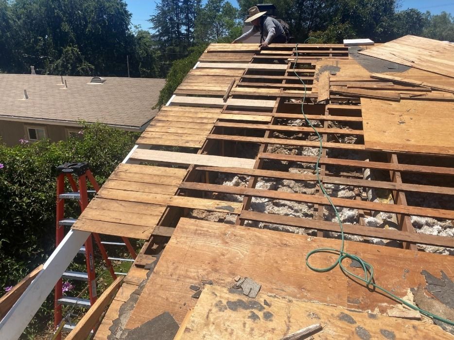 Roof being repaired: a worker on the roof, removing old wood, exposed beams, and a ladder.