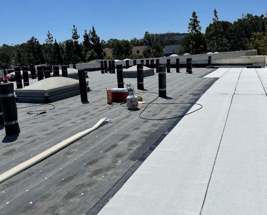 Flat commercial rooftop with black vent stacks and white insulation panels.