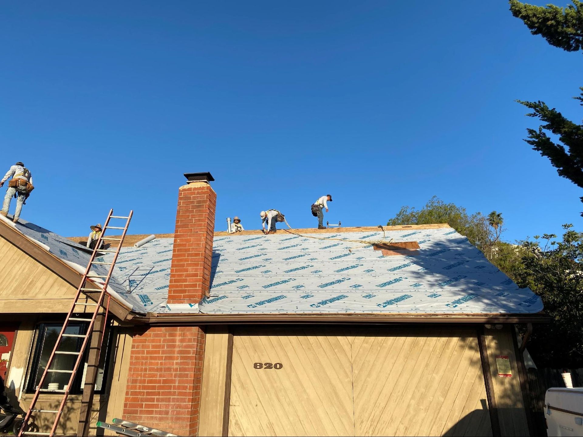 Roofers work on a house roof under a clear blue sky.